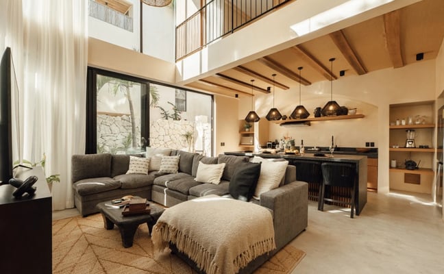 Modern patio with wooden deck, woven lounge chairs, slatted wood ceiling, and glass sliding doors opening to interior space, surrounded by tropical vegetation